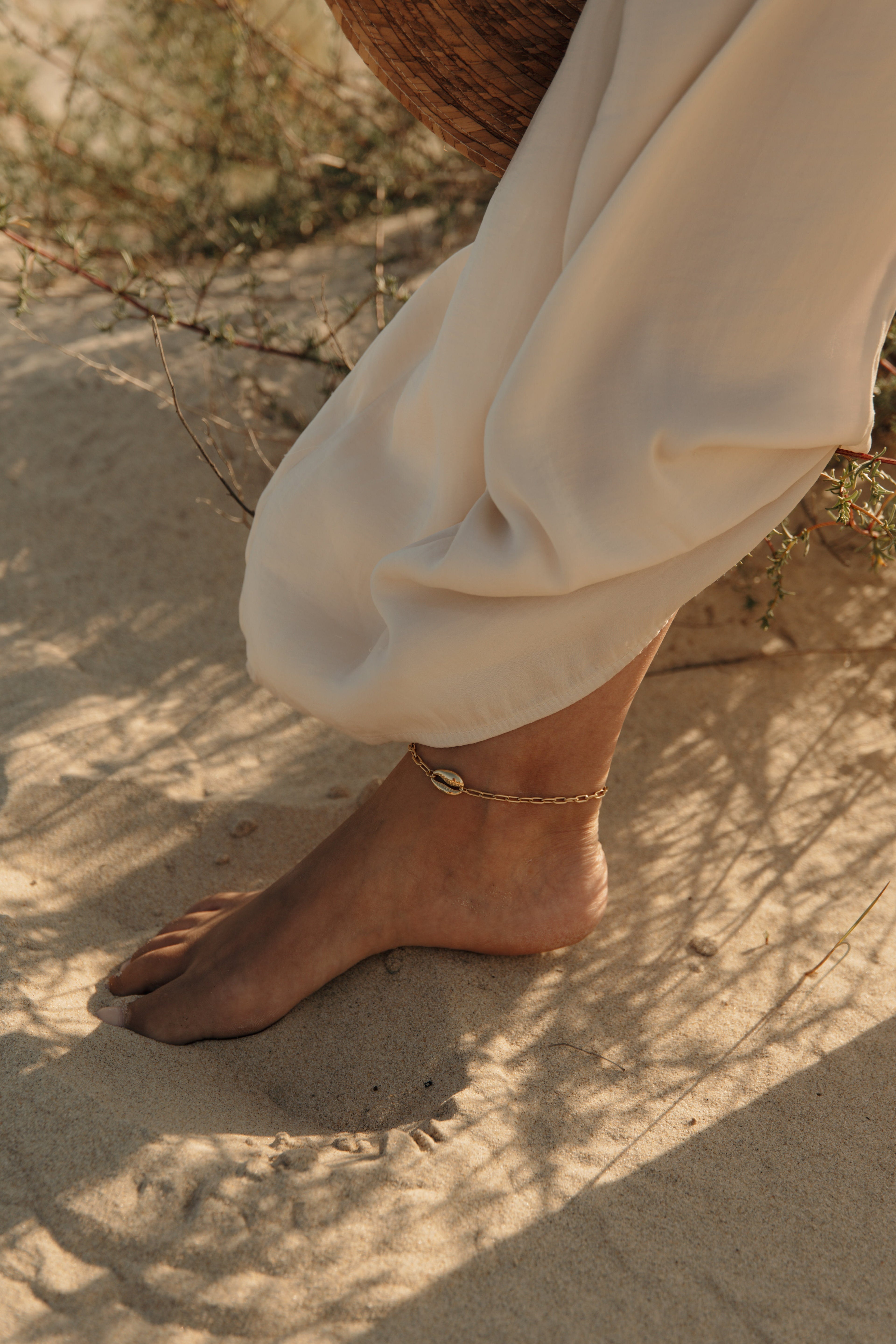 Chaîne de cheville dorée portée sur un pied dans le sable, pour un article sur les chaînes de chevilles et leur signification.