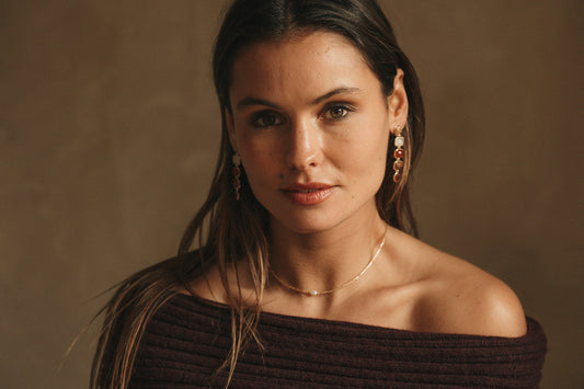 Femme portant des bijoux dorés Adalima, boucles d’oreilles et collier inspirés de la pierre de soleil, dans une lumière chaude et naturelle.