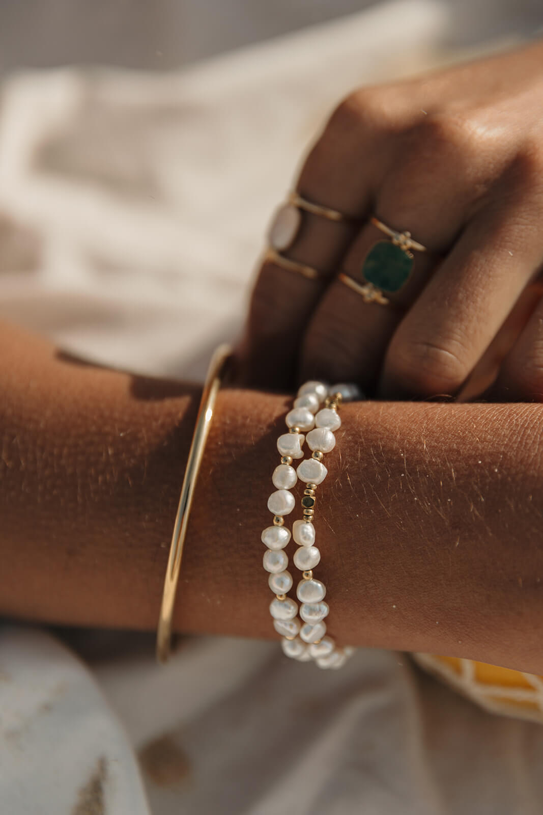 Bijouterie à Pau : bracelet perles blanches et bagues dorées portés au poignet.