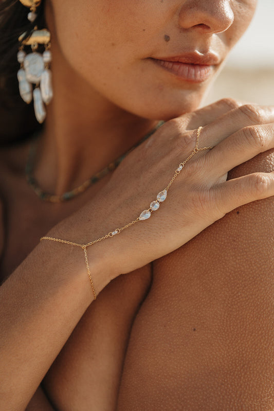 Chaîne de main en acier inoxydable, bijou fin avec perles blanches porté au poignet.
