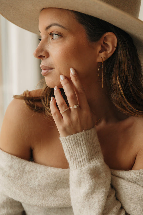 Femme portant la bague LOUVE dorée à zircons avec un pull en maille et un chapeau beige