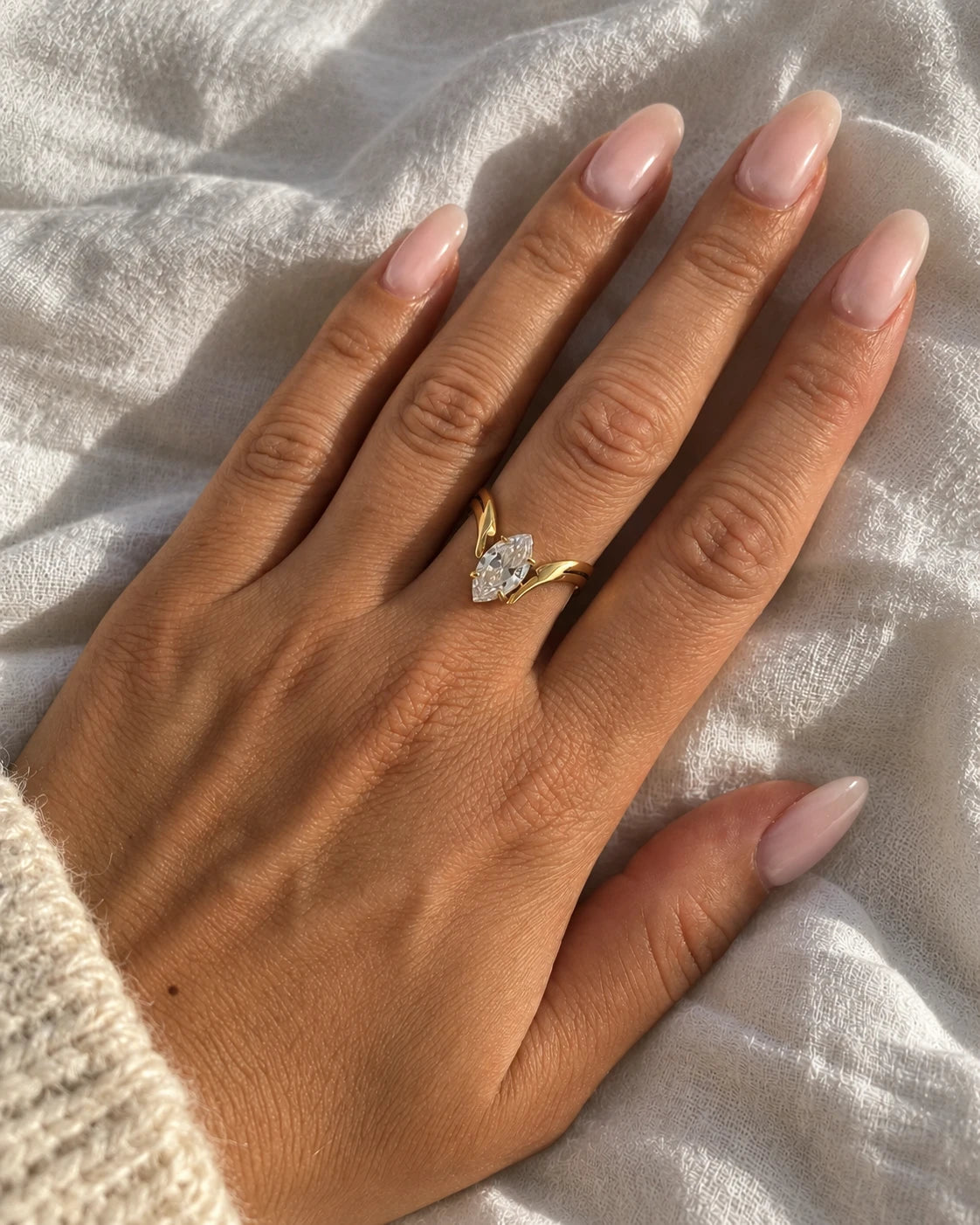 Bague SIENNA dorée à zircon navette portée, main posée sur un drap en lin